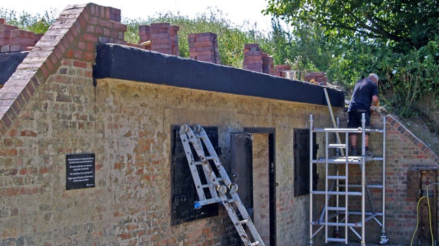 A bricklayer working on repairing the parapet wall of the Clem gun store, which was demolished when the site was covered over in the 1960s